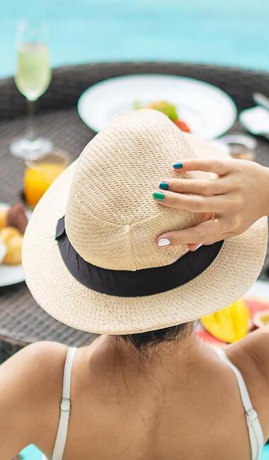 Donna con cappello di paglia in piscina davanti a un vassoio galleggiante con cibi e bevande per la colazione.