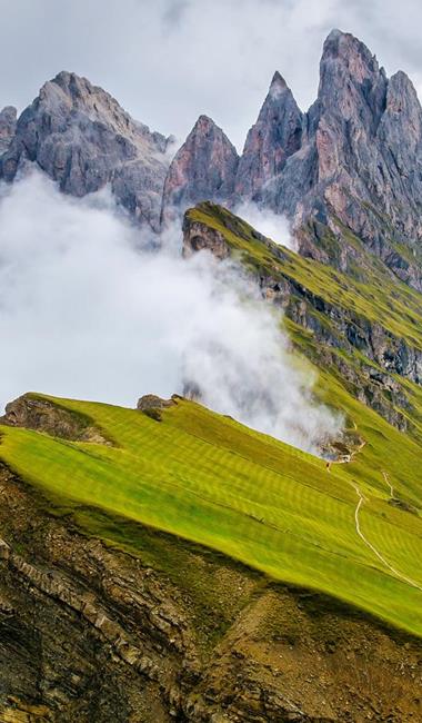 Grüne Bergwiesen am Seceda in Gröden mit markanten Felsgipfeln und Wolken im Hintergrund.