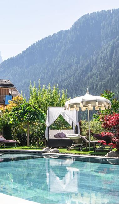 Piscina all'aperto con lettini e ombrelloni davanti a un paesaggio montano verde.