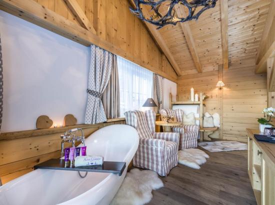 Der Wohnbereich der Mountain Suite mit freistehender Badewanne, Sitzecke und Bauernofen