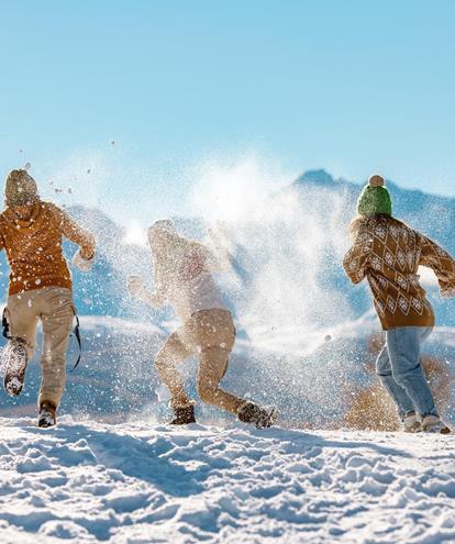 Tre persone si divertono nella neve con montagne innevate sullo sfondo.