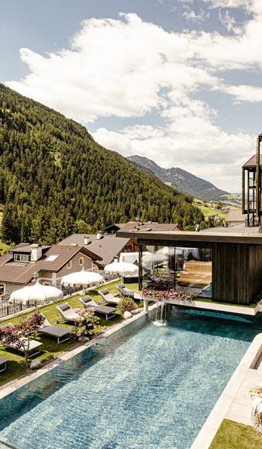 Vista esterna dell’Alpin Garden con piscina all’aperto, terrazza solarium e paesaggio montano.