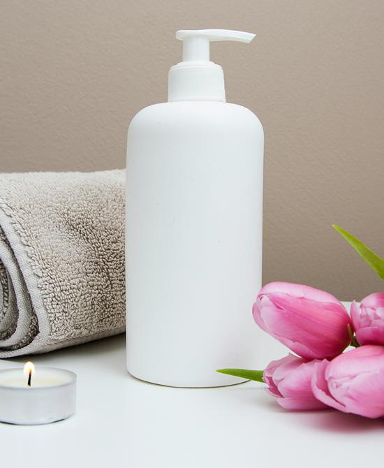 Pink tulips, a soap dispenser, a rolled-up towel and a lit tealight on a white surface.